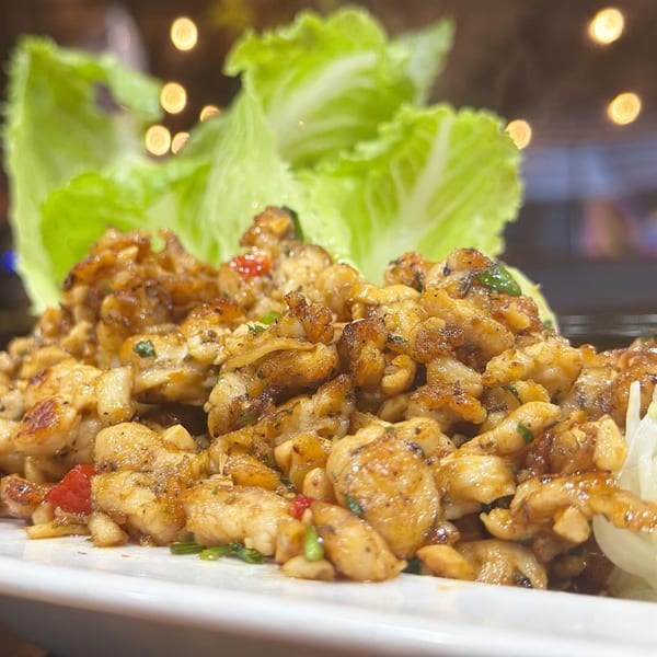 Close-up of golden-brown seafood pieces, possibly calamari, with green lettuce and bokeh lights in the background.
