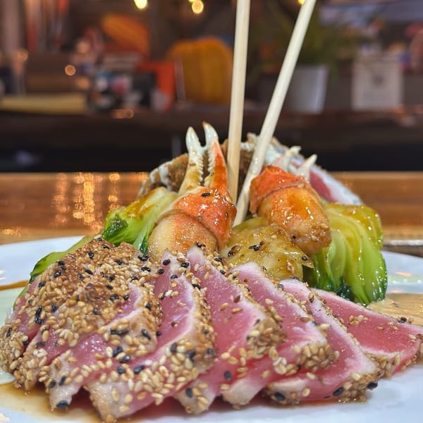 Seared tuna with sesame seeds, crab claws, and bok choy on a white plate at HOOKED.