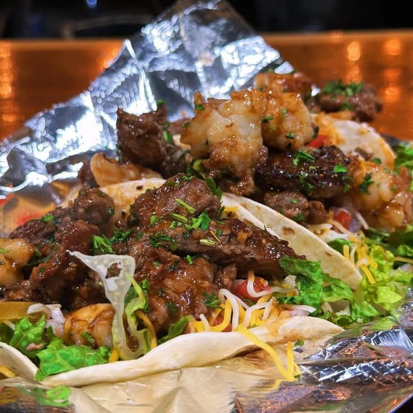 Close-up of Hooked's surf and turf tacos with steak, shrimp, lettuce, and cheese.