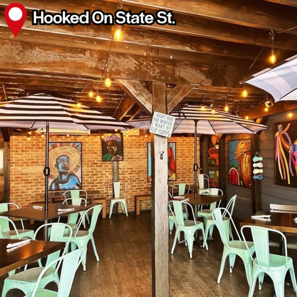 HOOKED restaurant interior with wooden beams, string lights, striped umbrellas, and mint green chairs.