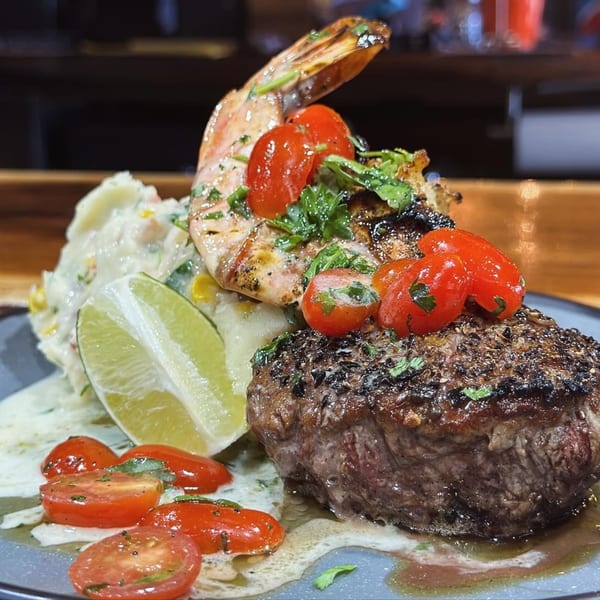 Grilled shrimp and steak with cherry tomatoes, lime, and mashed potatoes on a plate.