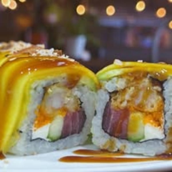 Two pieces of sushi with mango, tuna, shrimp tempura, and avocado, drizzled with sauce.