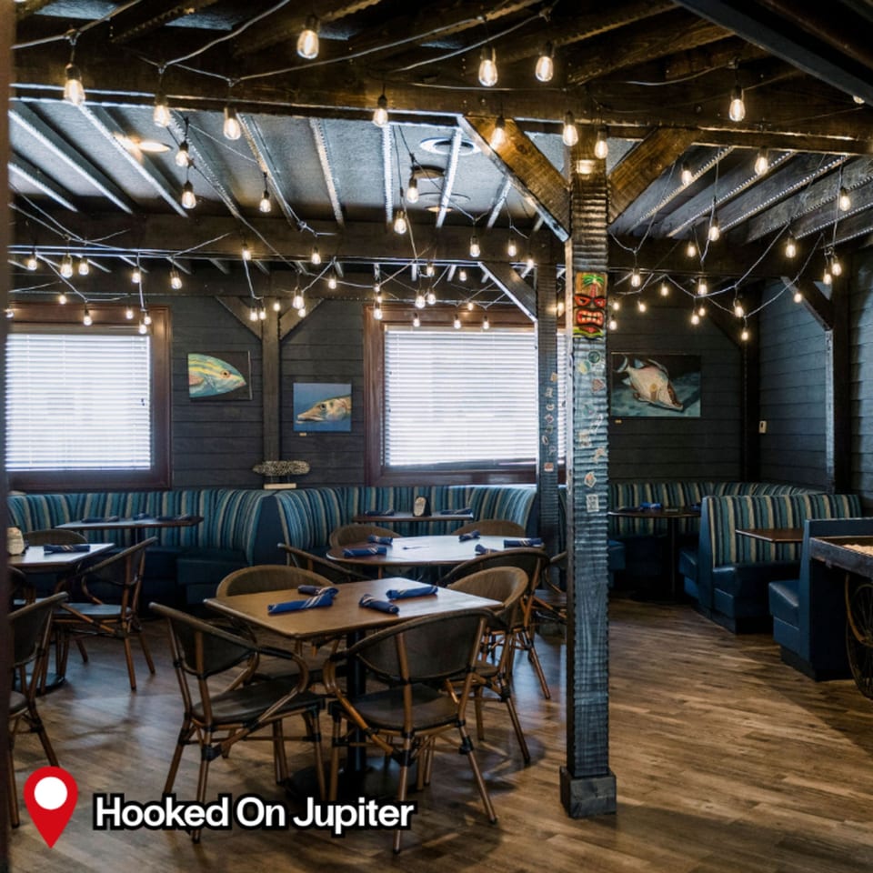 HOOKED restaurant interior with string lights, wooden tables, blue striped booths, and fish art.