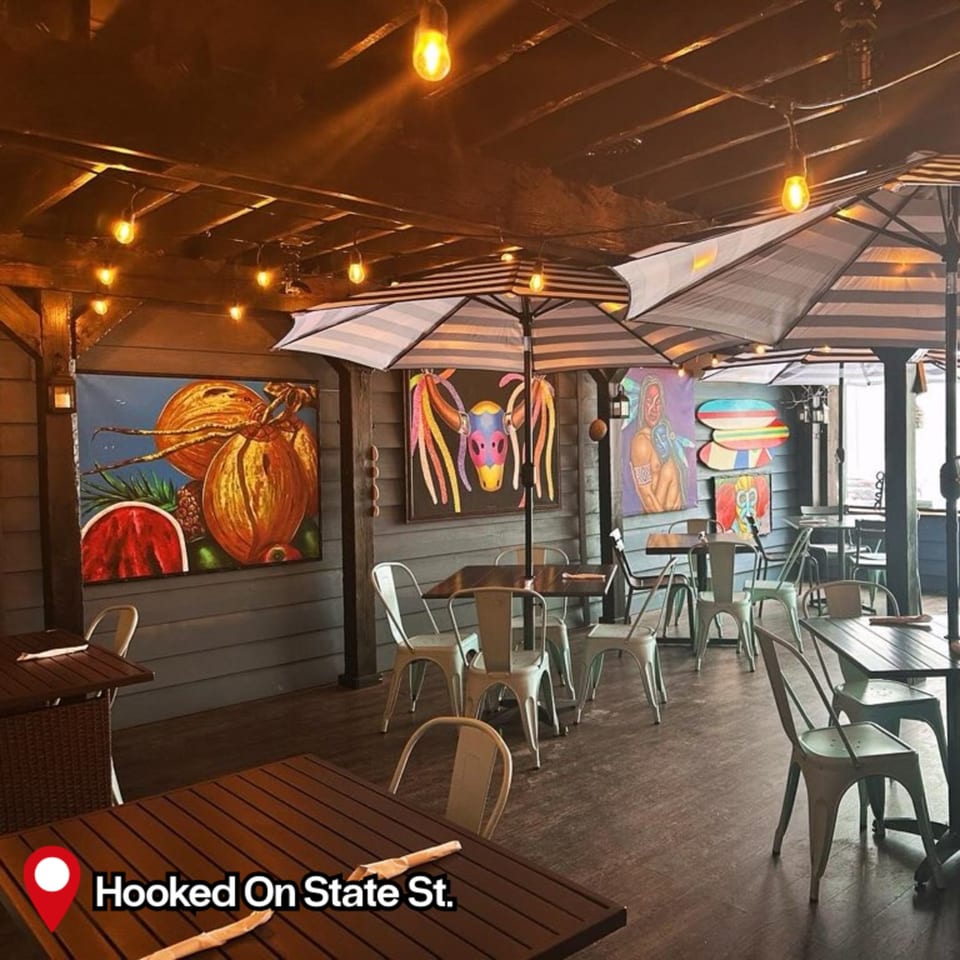 HOOKED's outdoor dining area with striped umbrellas, string lights, and colorful tropical art on blue walls.