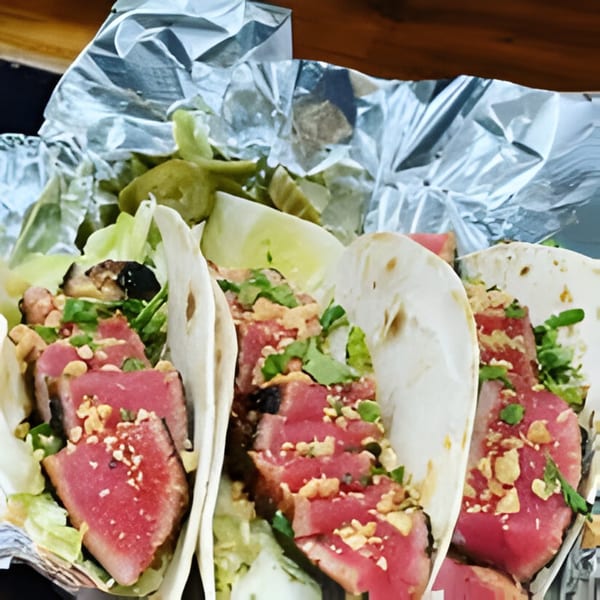 Three Hooked tuna tacos with seared fish, lettuce, and peanuts, served in foil.