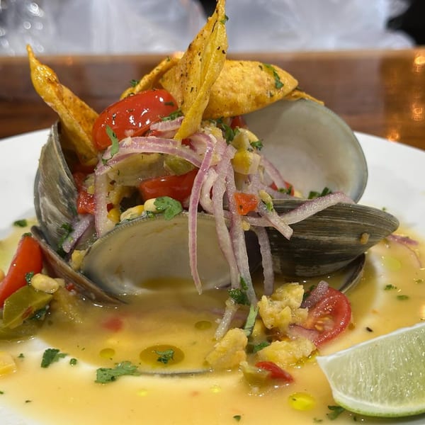 Clams on the half shell with red onion, cherry tomatoes, corn, and tortilla chips, garnished with lime.
