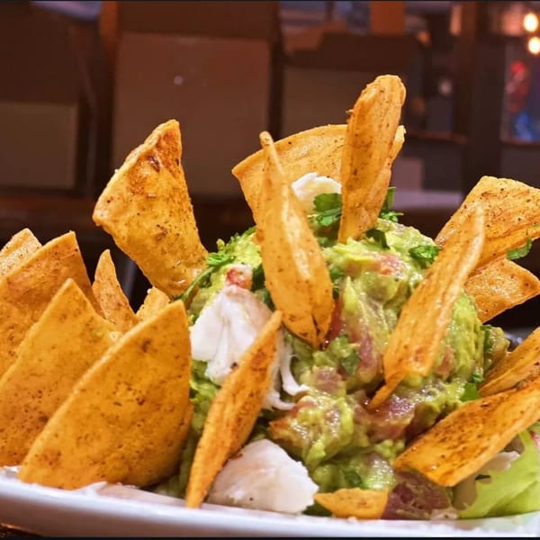 HOOKED's guacamole with tortilla chips and seafood, possibly crab or fish, in a white bowl.