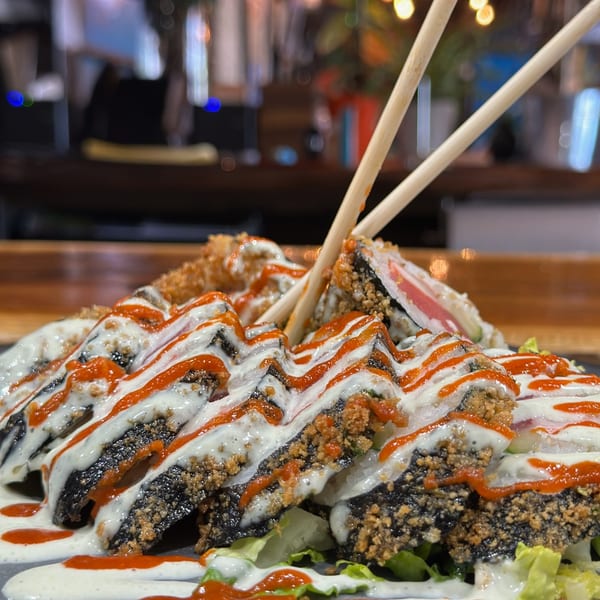 Crispy sushi rolls drizzled with white and red sauces, served on lettuce with chopsticks.